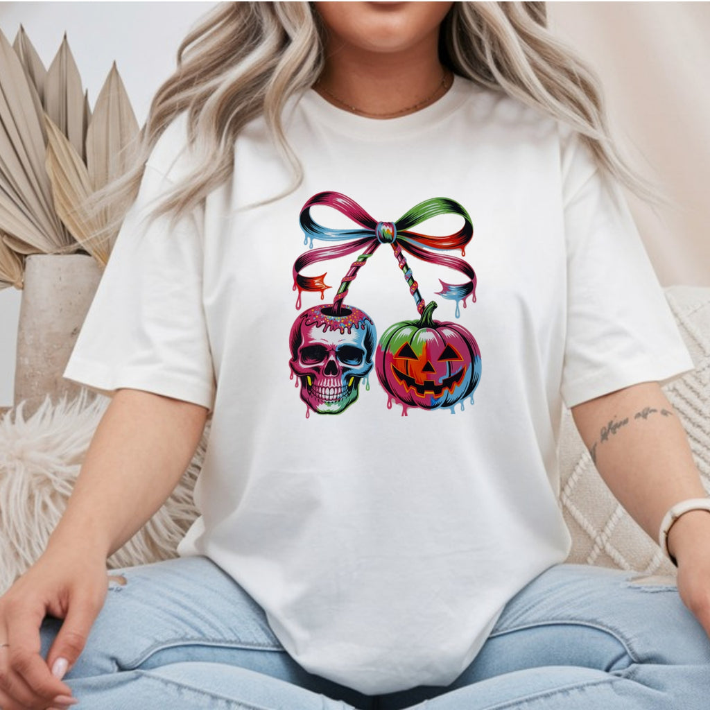 White Gildan Softstyle tee mockup with a drippy skull and jack-o-lantern hanging like cherries from a rainbow ribbon bow