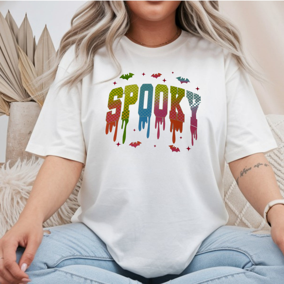 White Gildan Softstyle tee mockup with dripping neon checkered SPOOKY letters surrounded by bats and sparkles